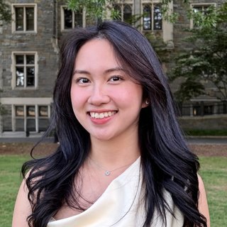 Evelyn Nguyen smiling, with long dark hair, in front of a stone building.