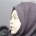 Nazmun Nahar Khanom in a purple headscarf, speaking into a microphone.